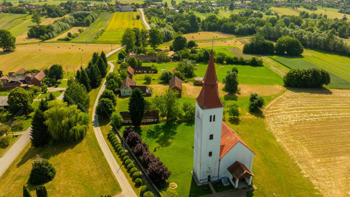 Charming aerial shot of a countryside church in Velika Trnovitica, Croatia, surrounded by fields and greenery.